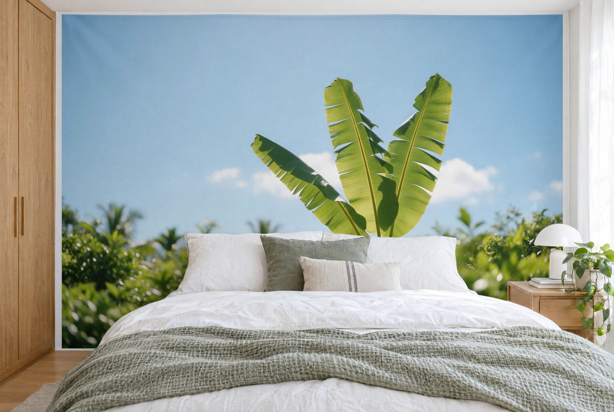 XXL printed fabric: three banana leaves against blue sky over a green garden, filling the wall behind the bed