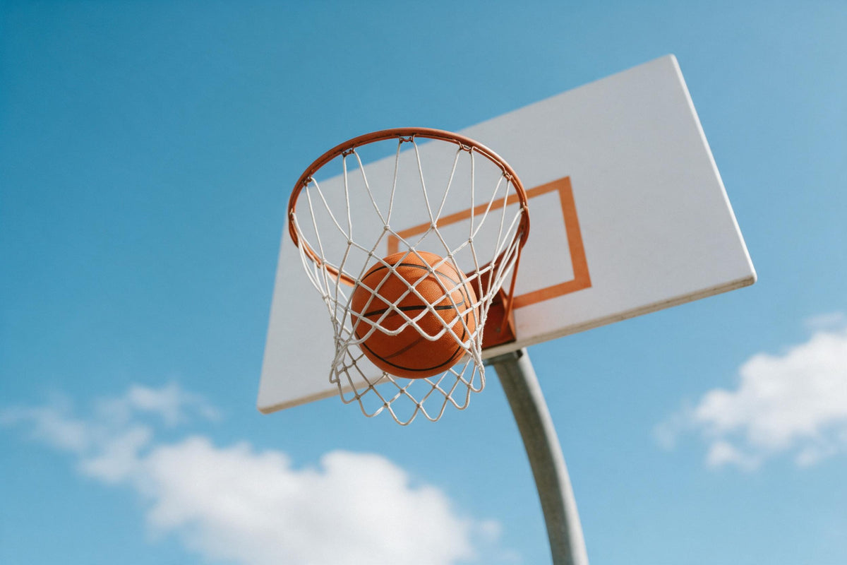 Basketball fällt durch das weisse Netz eines orangen Korbs vor blauem Himmel, als Wandtuch, auf Stoff gedruckt – Orange, Blau
