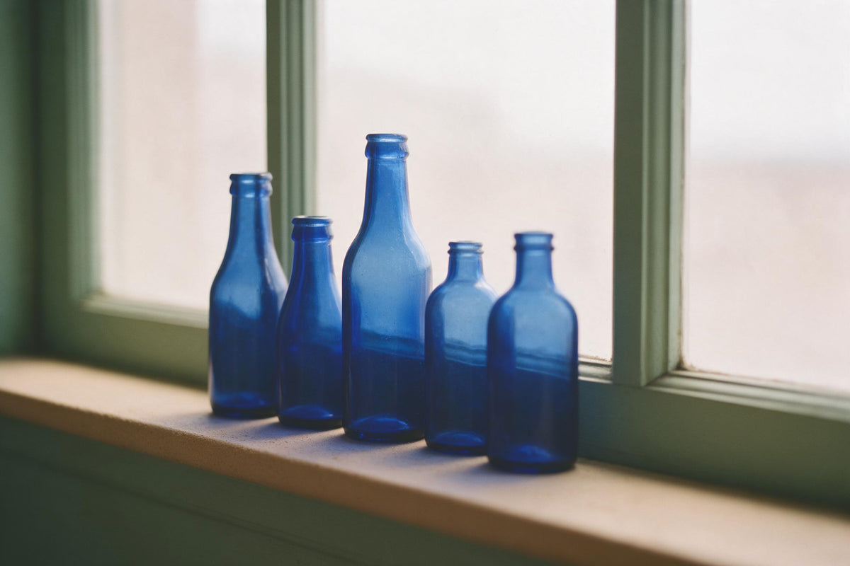 Rangée de bouteilles en verre bleu sur rebord clair devant cadre vert, tenture murale imprimée sur tissu – bleu et beige