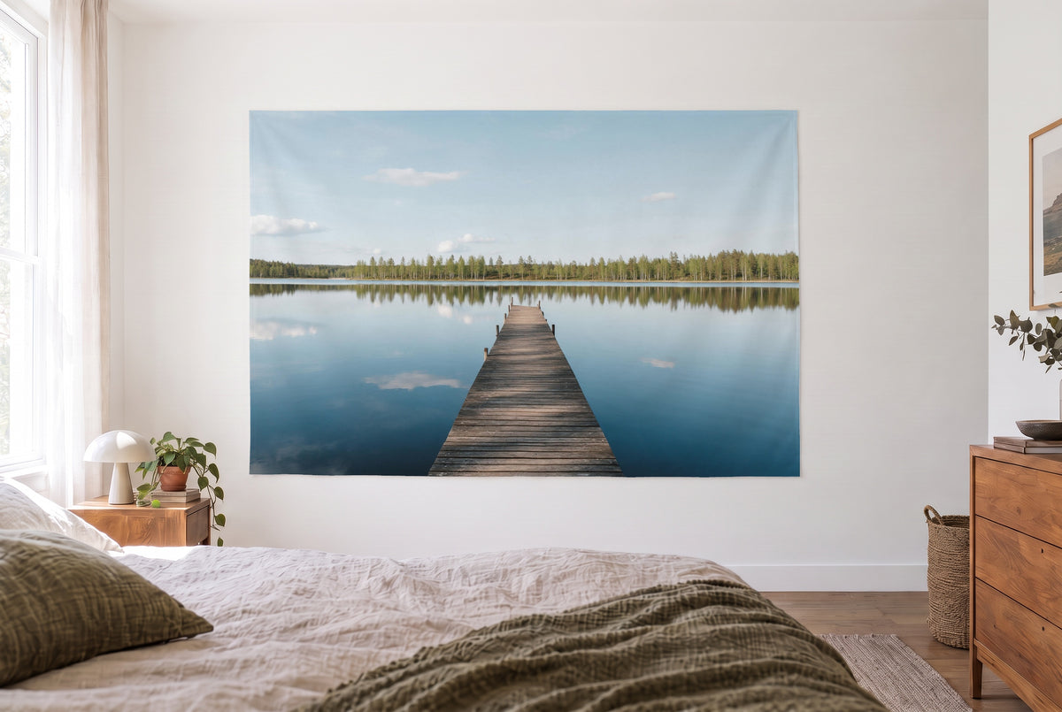 Tenture ponton sur un lac paisible dans la chambre claire face au lit, commode en bois à droite – bleu et vert