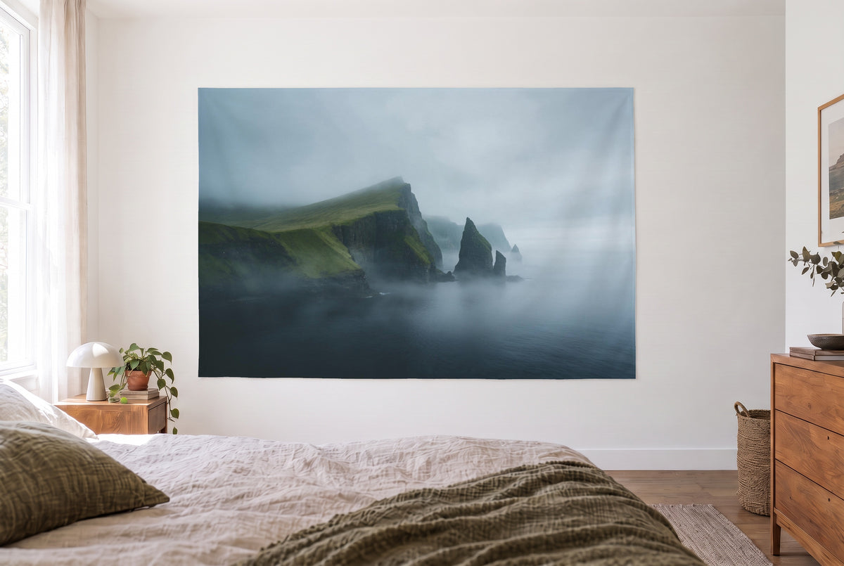 Steep green northern-sea cliffs tapestry in the bright bedroom opposite the bed, wooden dresser at right – green and grey