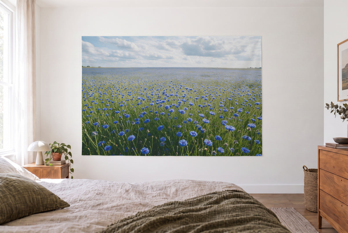 Wandtuch Kornblumenfeld unter Wolkenhimmel im hellen Schlafzimmer gegenüber dem Bett, rechts eine Holzkommode – Blau und Grün