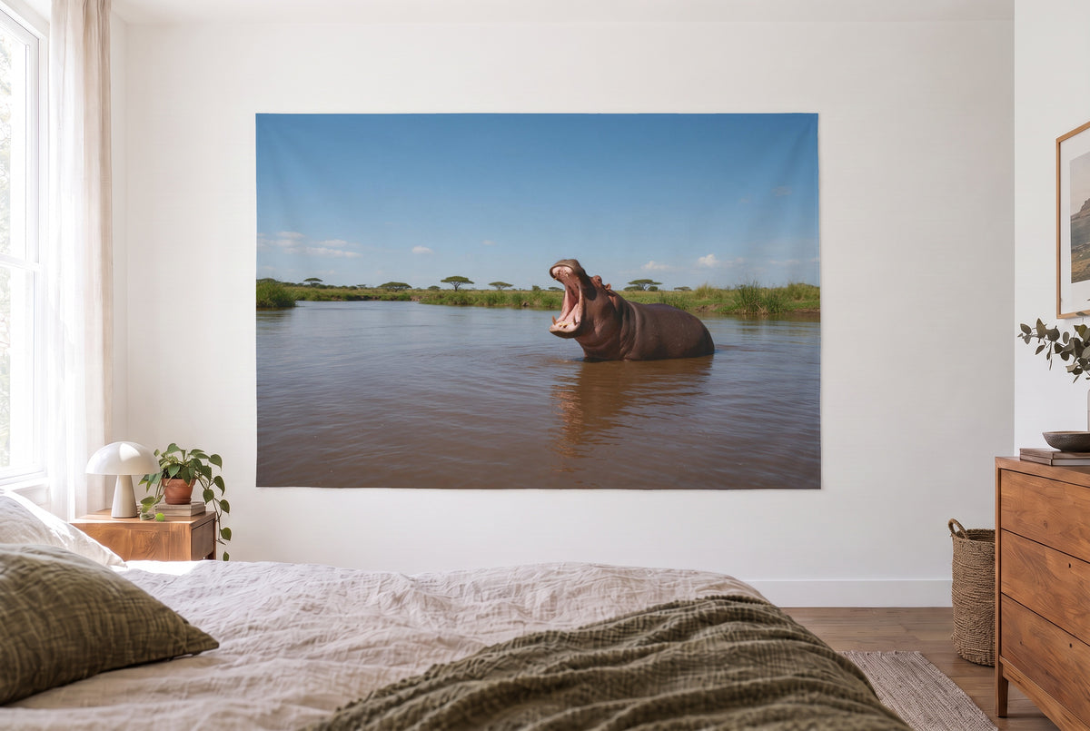 Hippo with Open Mouth in the River tapestry in the bright bedroom opposite the bed, wooden dresser at right – brown blue