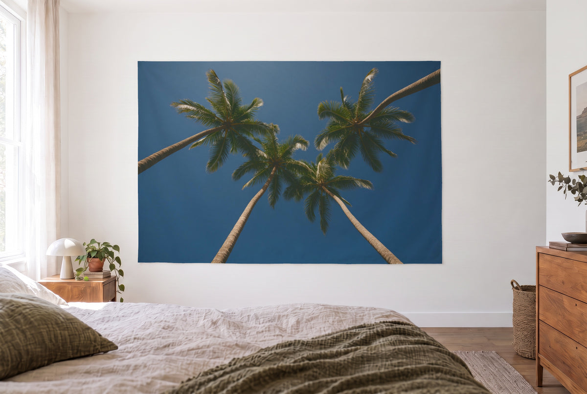 Wandtuch Palmen vor blauem Himmel im hellen Schlafzimmer gegenüber dem Bett, rechts eine Holzkommode – Blau und Grün