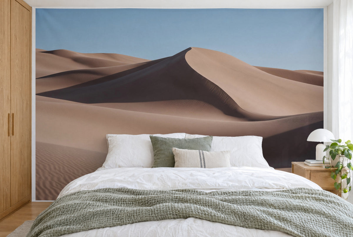Bedruckter Stoff im XXL-Format: geschwungene Sanddünen unter blauem Himmel, wandfüllend hinter dem Bett