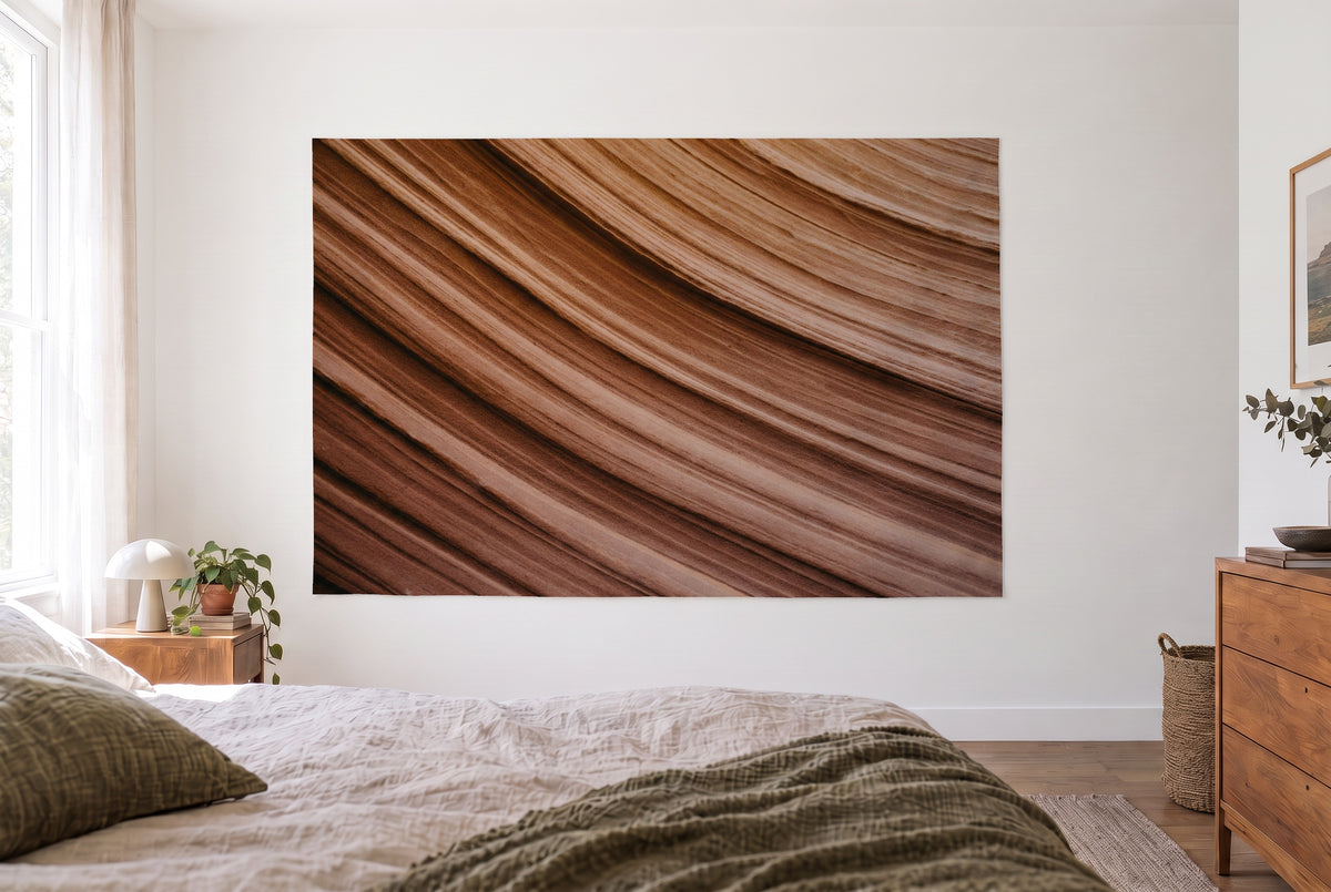Curved sandstone layers tapestry in a bright bedroom opposite the bed, wooden dresser at right – brown and ochre