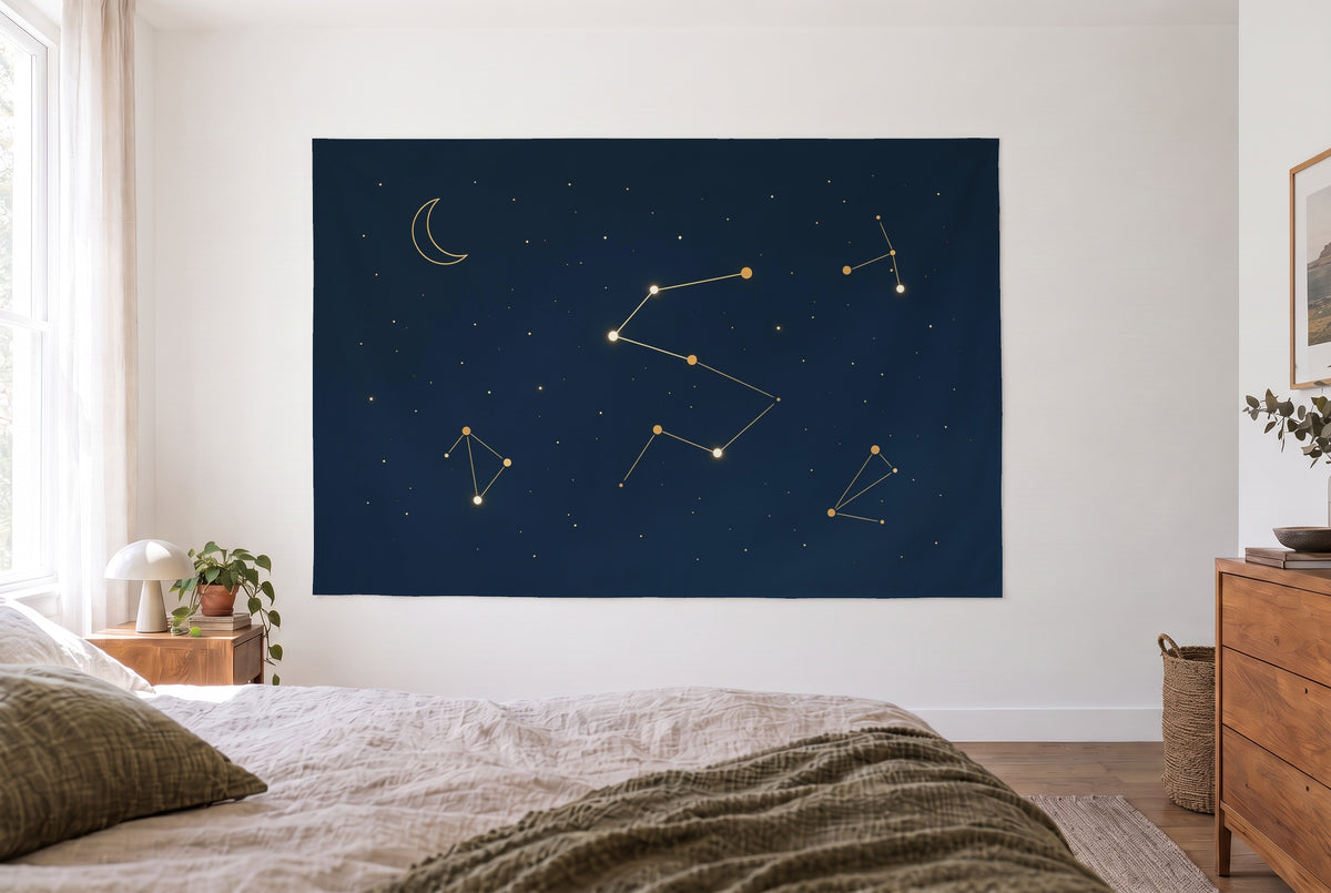 Night sky constellations tapestry in the bright bedroom opposite the bed, wood dresser on the right – blue and gold
