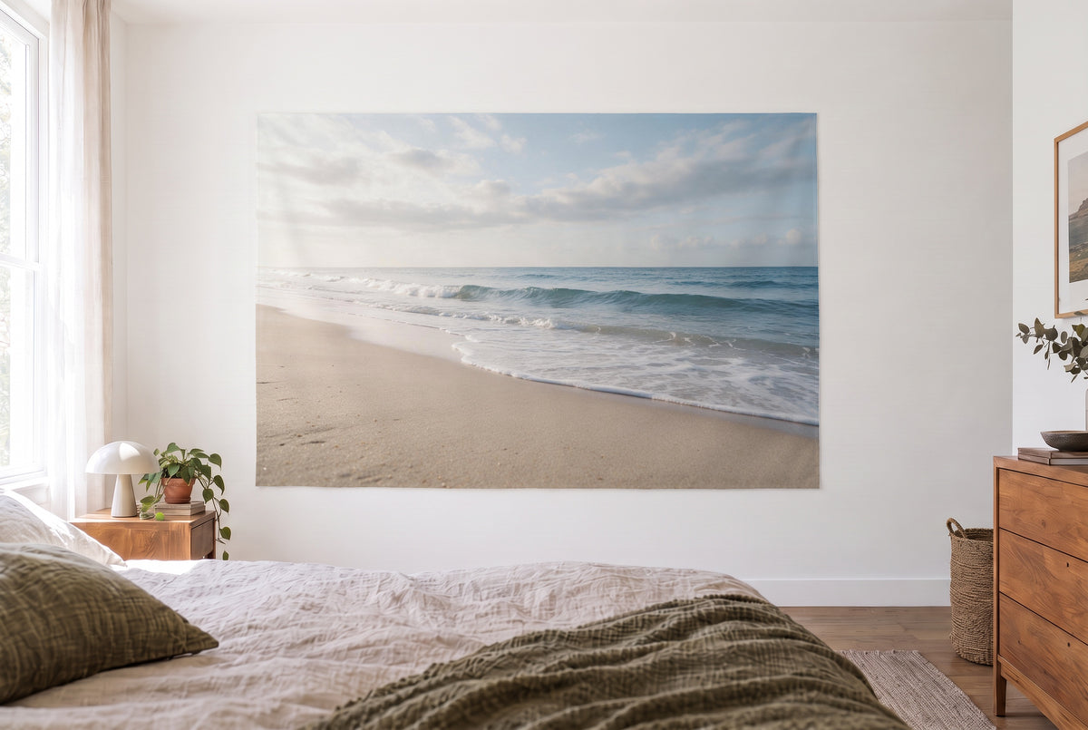 Wandtuch Strand mit sanften Wellen im hellen Schlafzimmer gegenüber dem Bett, rechts eine Holzkommode – Beige und Blau