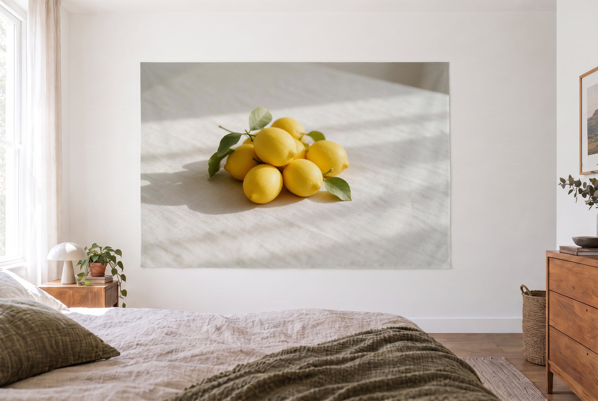 Wandtuch Zitronen mit Blättern auf Leinen im hellen Schlafzimmer gegenüber dem Bett, rechts eine Holzkommode – Gelb und Weiss