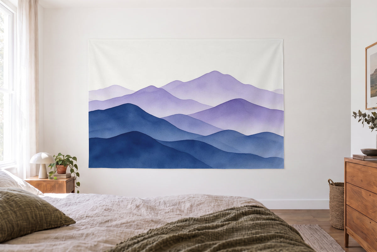 Mountains color gradient watercolor tapestry in the bright bedroom opposite the bed, wooden dresser at right – blue violet