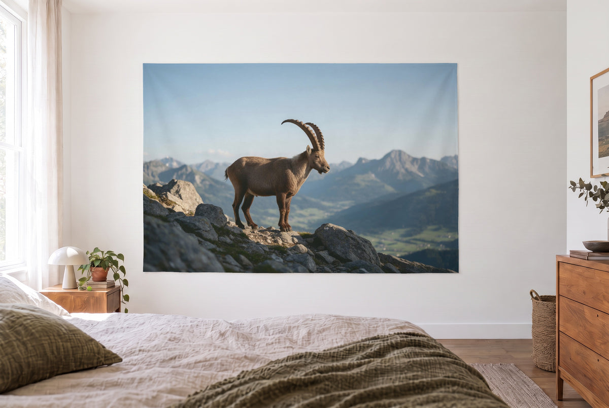 Wandtuch Steinbock auf dem Felsgrat im hellen Schlafzimmer gegenüber dem Bett, rechts eine Holzkommode – Braun Grau Blau