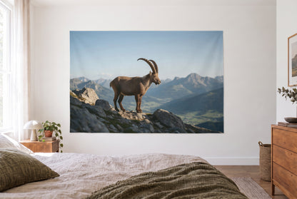 Wandtuch Steinbock auf dem Felsgrat im hellen Schlafzimmer gegenüber dem Bett, rechts eine Holzkommode – Braun Grau Blau