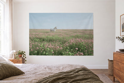 Tenture murale licorne prairie fleurie dans la chambre claire face au lit, commode en bois à droite – rose et vert