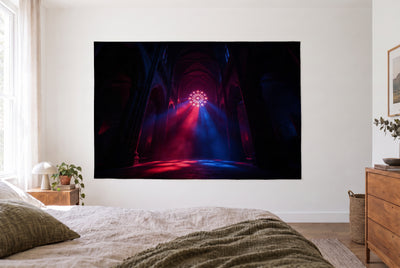 Tenture cathédrale gothique à contre-jour dans une chambre claire face au lit, commode en bois à droite – rouge et bleu