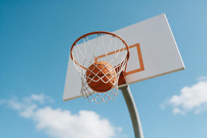 Basketball fällt durch das weisse Netz eines orangen Korbs vor blauem Himmel, als Wandtuch, auf Stoff gedruckt – Orange, Blau