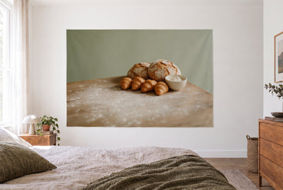Tenture pain de campagne et croissants dans une chambre claire face au lit, commode en bois à droite – brun et vert sauge