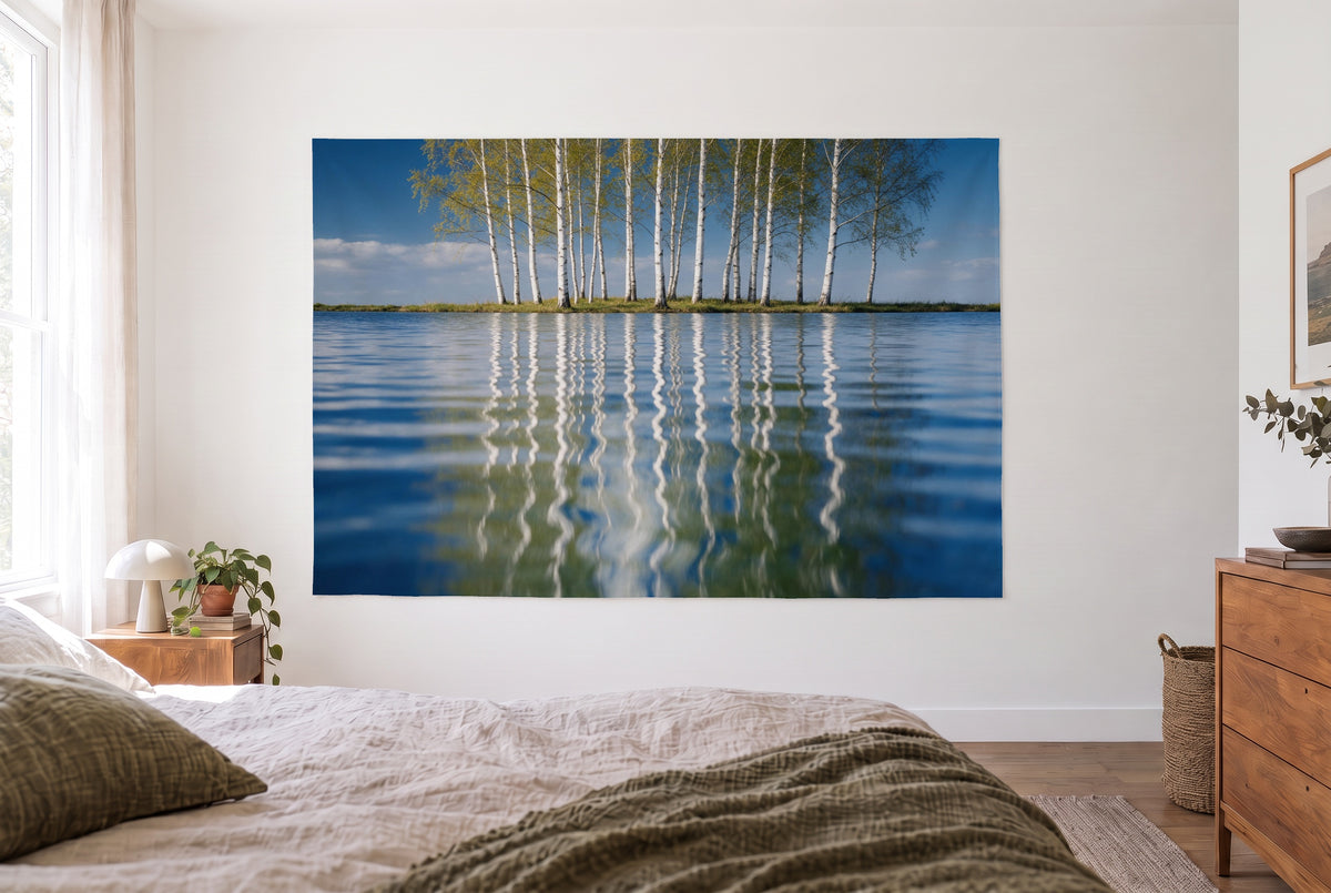Wandtuch Birken spiegeln sich im Wasser im hellen Schlafzimmer gegenüber dem Bett, rechts eine Holzkommode – Blau und Weiss