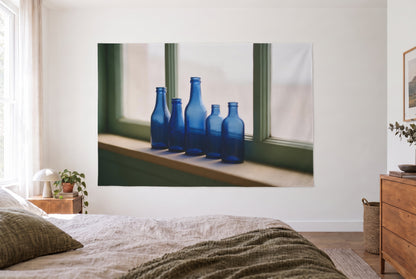 Tenture bouteilles en verre bleu à la fenêtre dans une chambre claire face au lit, commode en bois à droite – bleu