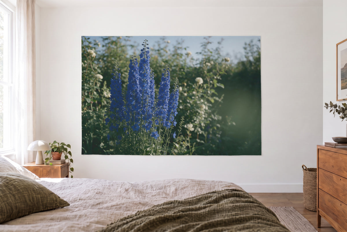 Blue delphinium in a cottage garden tapestry in a bright bedroom opposite the bed, wooden dresser at right – blue