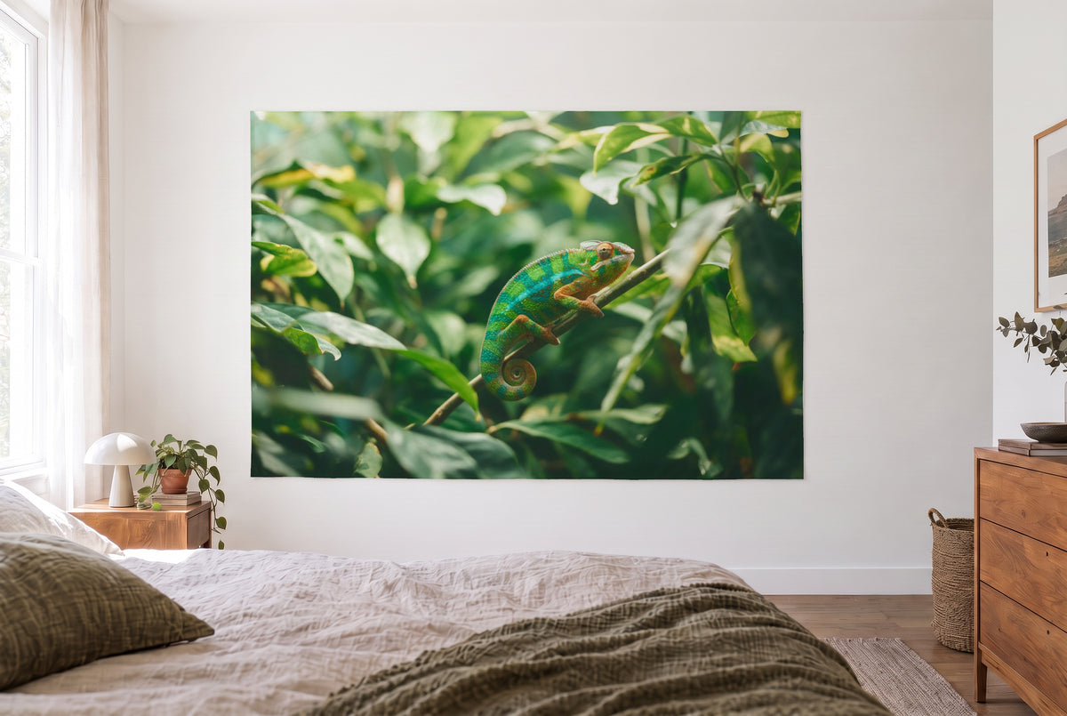 Tenture caméléon sur la branche dans une chambre claire face au lit, commode en bois à droite – vert et orange
