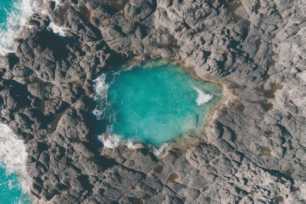 Rock pool with turquoise water between dark coastal rocks from above, tapestry printed on fabric – turquoise and grey