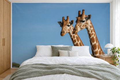 XXL printed fabric: two giraffe heads at right against a wide blue sky, filling the wall behind the bed
