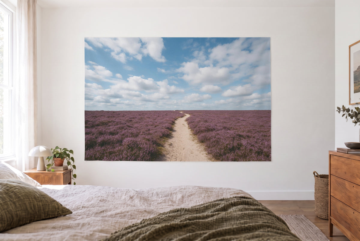 Wandtuch Blauer Wolkenhimmel über Heide im hellen Schlafzimmer gegenüber dem Bett, rechts eine Holzkommode – Blau und Violett