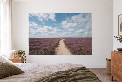 Wandtuch Blauer Wolkenhimmel über Heide im hellen Schlafzimmer gegenüber dem Bett, rechts eine Holzkommode – Blau und Violett