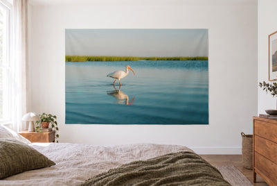Wandtuch Ibis im flachen Wasser im hellen Schlafzimmer gegenüber dem Bett, rechts eine Holzkommode – Türkis und Weiss