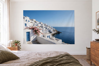 Tenture village côtier en Grèce dans une chambre claire face au lit, commode en bois à droite – blanc et bleu