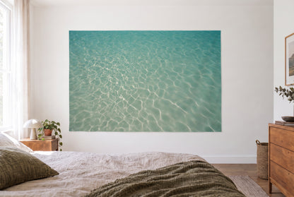 Wandtuch Lichtnetz auf türkisem Wasser im hellen Schlafzimmer gegenüber dem Bett, rechts eine Holzkommode – Blau und Grün