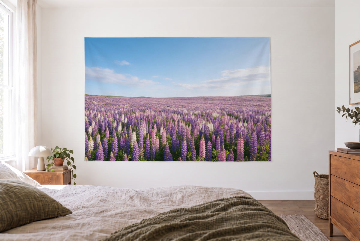 Tapiz campo de lupinos hasta el horizonte en un cuarto claro frente a la cama, cómoda de madera a la derecha – violeta y azul