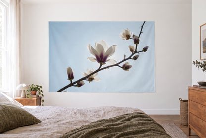 Wandtuch Magnolienzweig vor Himmel im hellen Schlafzimmer gegenüber dem Bett, rechts eine Holzkommode – Weiss und Blau