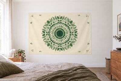 Tenture mandala forestier vert dans une chambre claire face au lit, une commode en bois à droite – vert et beige