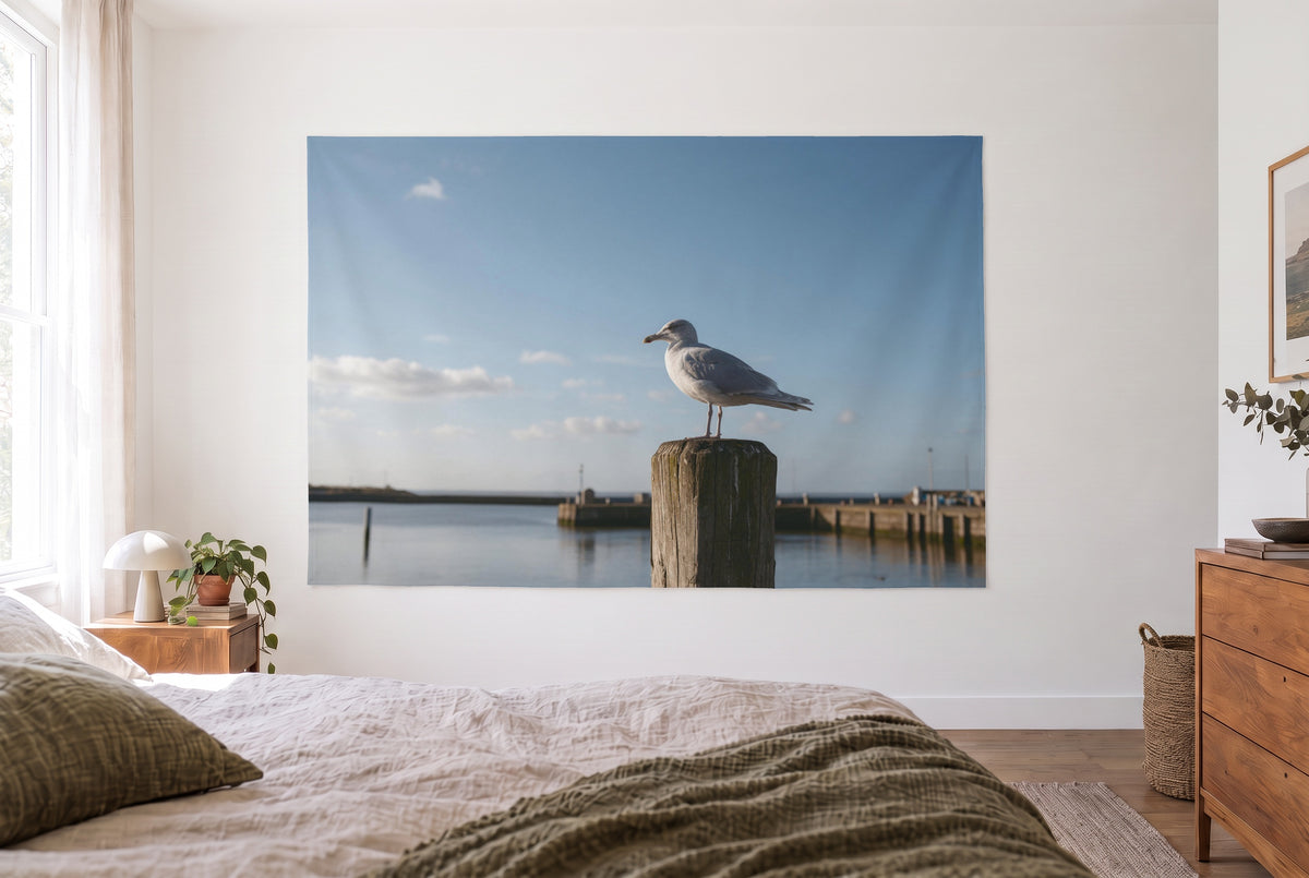 Wandtuch Möwe auf dem Hafenpfahl im hellen Schlafzimmer gegenüber dem Bett, rechts eine Holzkommode – Grau und Blau