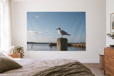 Wandtuch Möwe auf dem Hafenpfahl im hellen Schlafzimmer gegenüber dem Bett, rechts eine Holzkommode – Grau und Blau