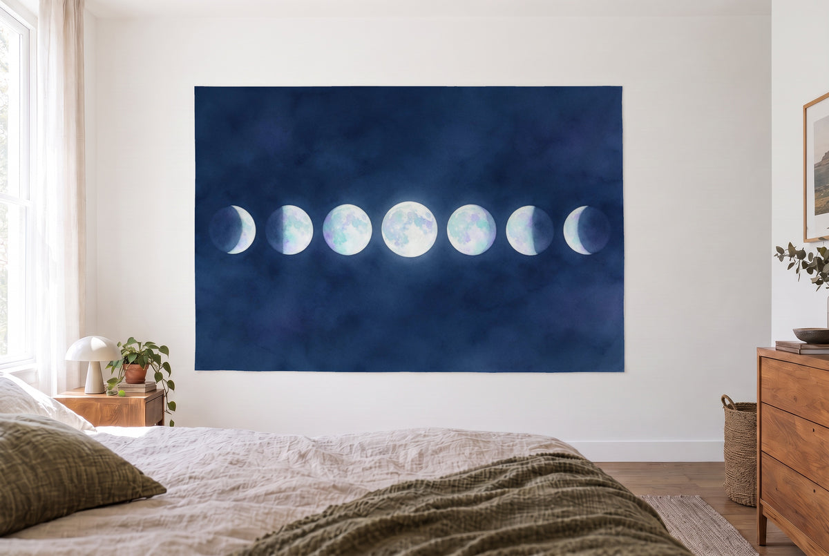 Moon phases in opal tones tapestry in the bright bedroom opposite the bed, wooden dresser at right – blue and white