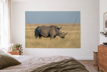 Wandtuch Nashorn in der Steppe im hellen Schlafzimmer gegenüber dem Bett, rechts eine Holzkommode – Gold, Grau und Blau