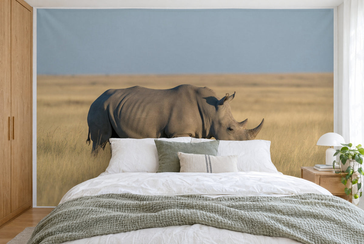 Bedruckter Stoff im XXL-Format: Nashorn links der Mitte im goldenen Steppengras, darüber Himmel, wandfüllend hinter dem Bett