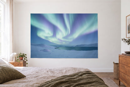 Wandtuch Nordlichter über Schneehügeln im hellen Schlafzimmer gegenüber dem Bett, rechts eine Holzkommode – Blau und Grün