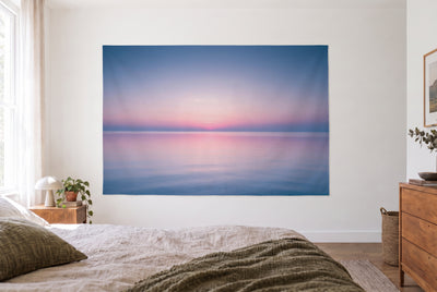 Tapiz cielo rosa sobre mar en calma en dormitorio claro frente a la cama, cómoda de madera a la derecha – rosa y azul