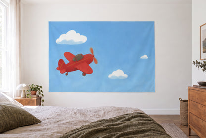 Red Propeller Plane in the Sky tapestry in the bright bedroom opposite the bed, wooden dresser at right – red and blue