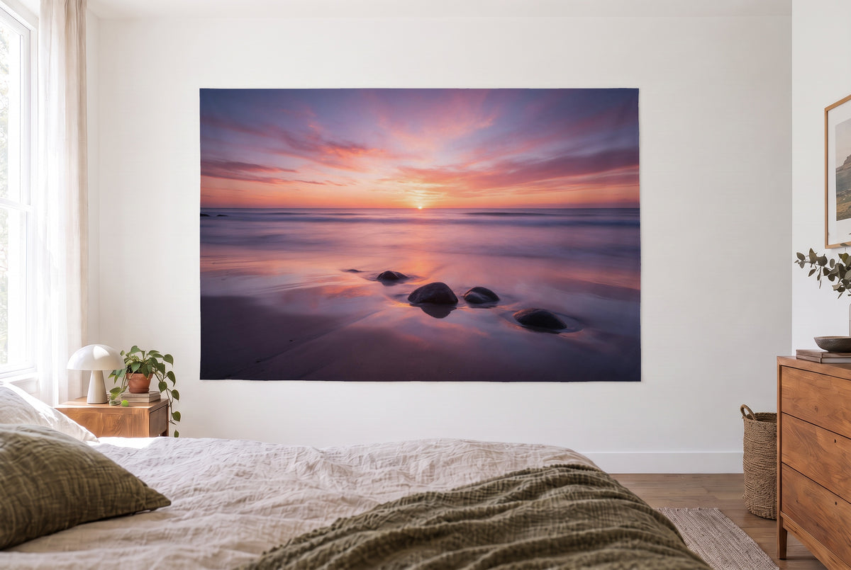 Wandtuch Sonnenuntergang am Meer im hellen Schlafzimmer gegenüber dem Bett, rechts eine Holzkommode – Orange Rosa Violett