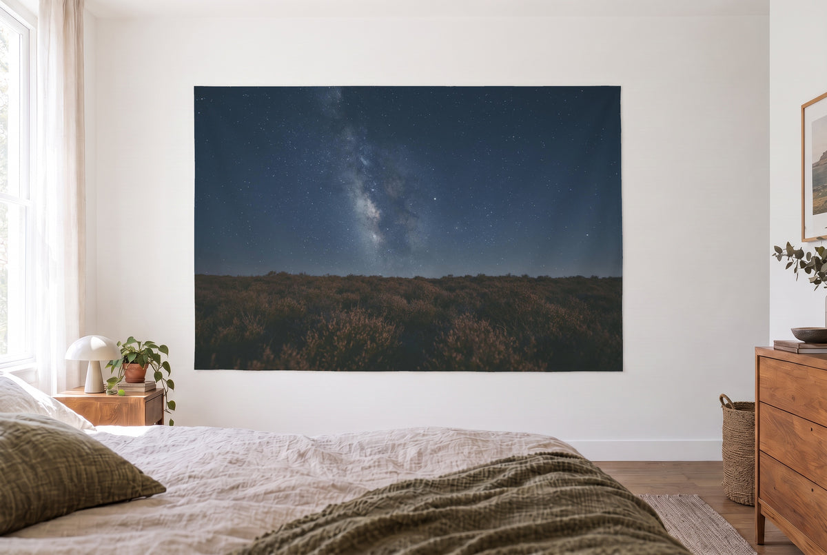 Tapiz cielo estrellado sobre el brezal en el dormitorio claro frente a la cama, cómoda de madera a la derecha – azul y marrón