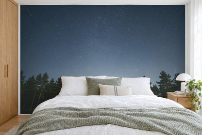 Bedruckter Stoff im XXL-Format: klarer Sternenhimmel über Kiefernkronen, wandfüllend hinter dem Bett