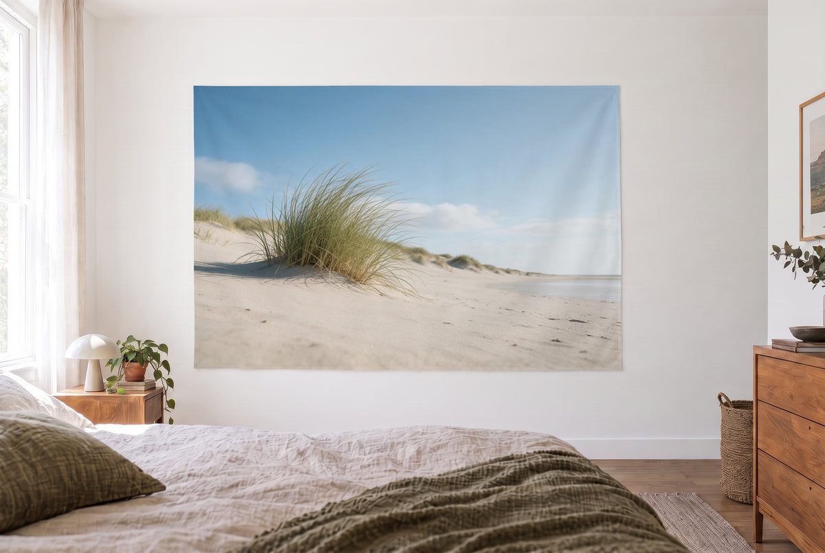 Marram grass in the dunes tapestry in a bright bedroom opposite the bed, wooden dresser at right – sand beige and light blue