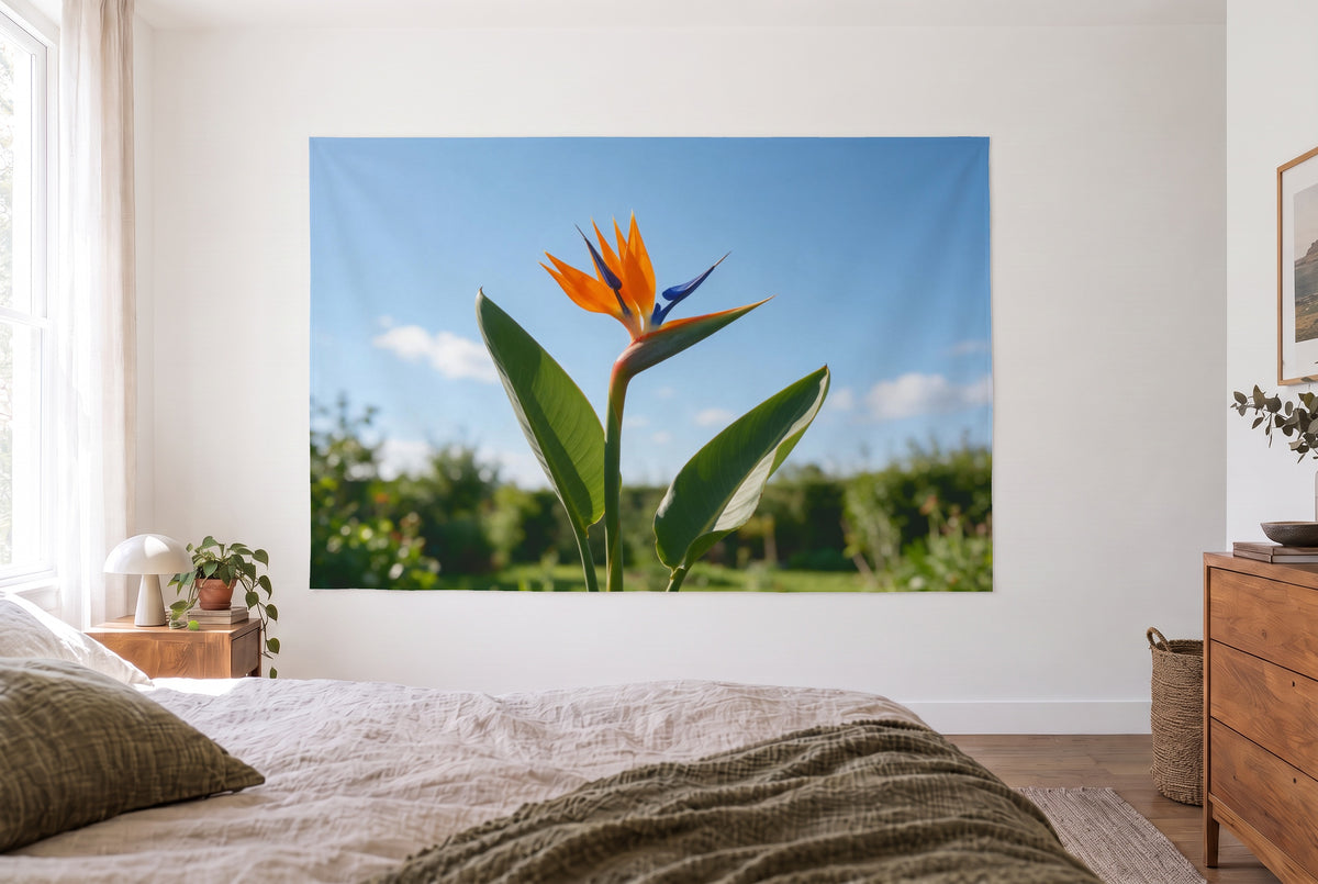 Wandtuch Strelitzienblüte vor Himmel im hellen Schlafzimmer gegenüber dem Bett, rechts eine Holzkommode – Orange und Blau