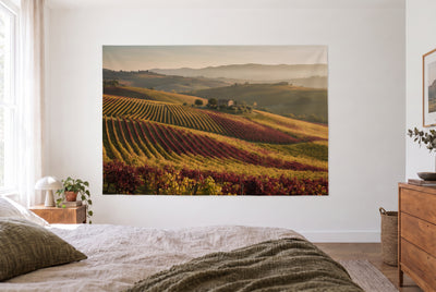 Wandtuch Weinberge im Herbstlicht im hellen Schlafzimmer gegenüber dem Bett, rechts eine Holzkommode – Weinrot und Gold