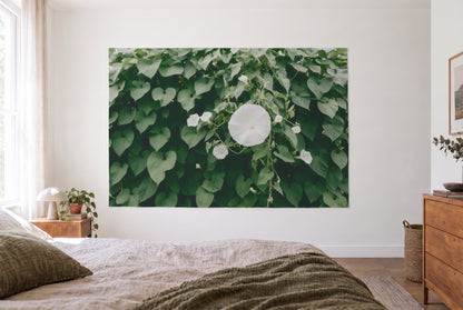 White moonflower blossoms tapestry in a bright bedroom opposite the bed, wooden dresser on the right – white and green