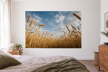 Wandtuch Weizenfeld unter Wolkenhimmel im hellen Schlafzimmer gegenüber dem Bett, rechts eine Holzkommode – Gold und Blau